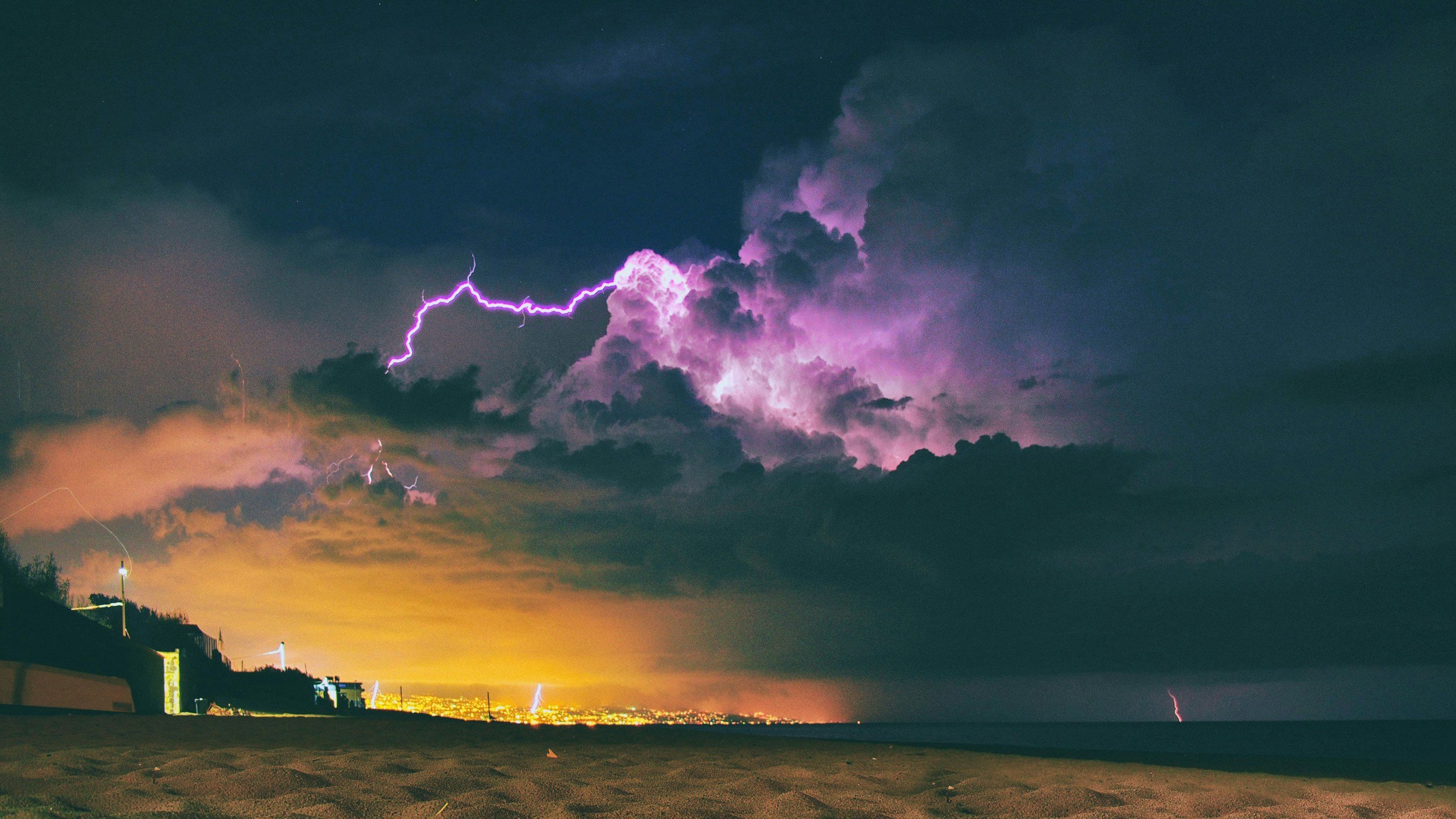Stürmische Gewitternacht über dem Strand mit Blitzschlägen in dunklem Himmel, Wolken in Lila und Orange, Blick auf das Meer und den Horizont